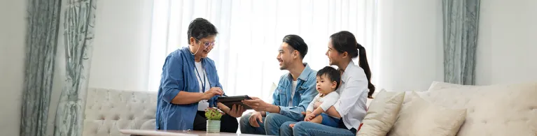 A life insurance policy manager shares a digital device with a family and their child while they sit on a couch in an office. 