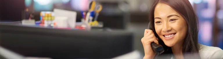 A young office worker is chatting happily on the phone in a large office.