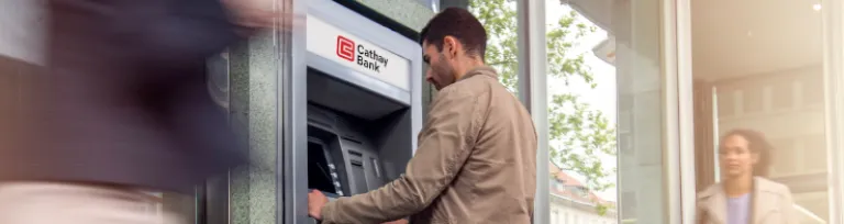 Focus on man standing in front of an ATM machine on a city street, defocused incidental people.