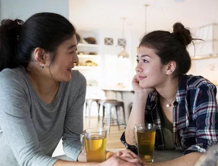 Mother and teenage daughter holding hands drinking tea.