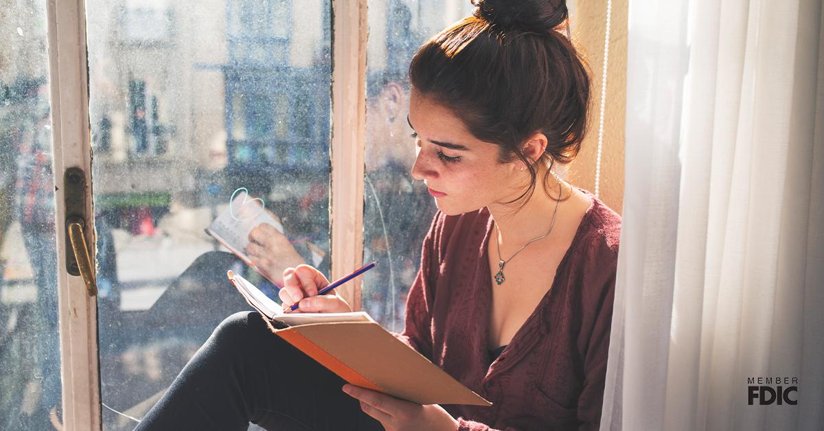 Young woman writes diary next to the window.