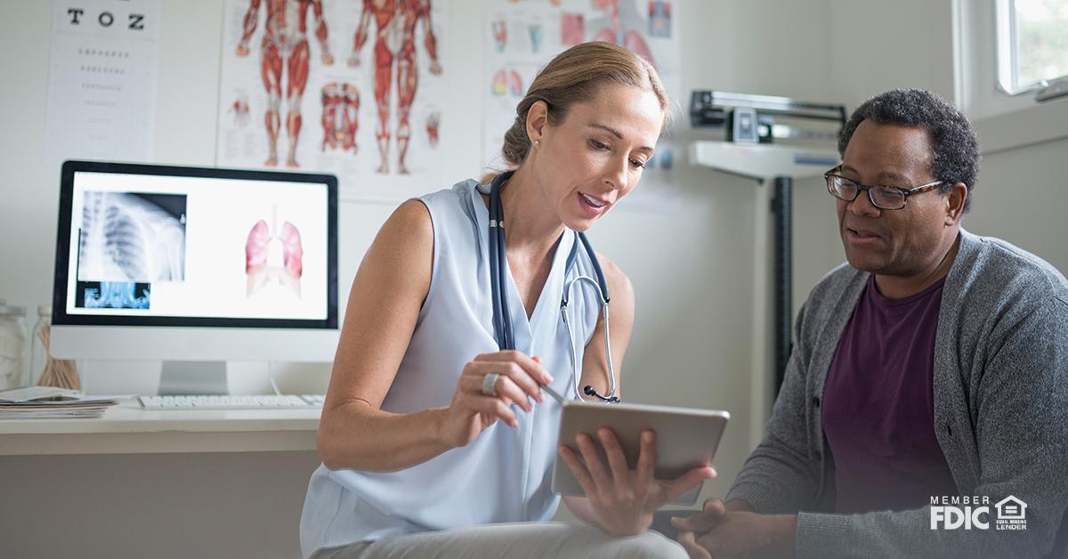 Female doctor with digital tablet talking with senior male patient in examination room.