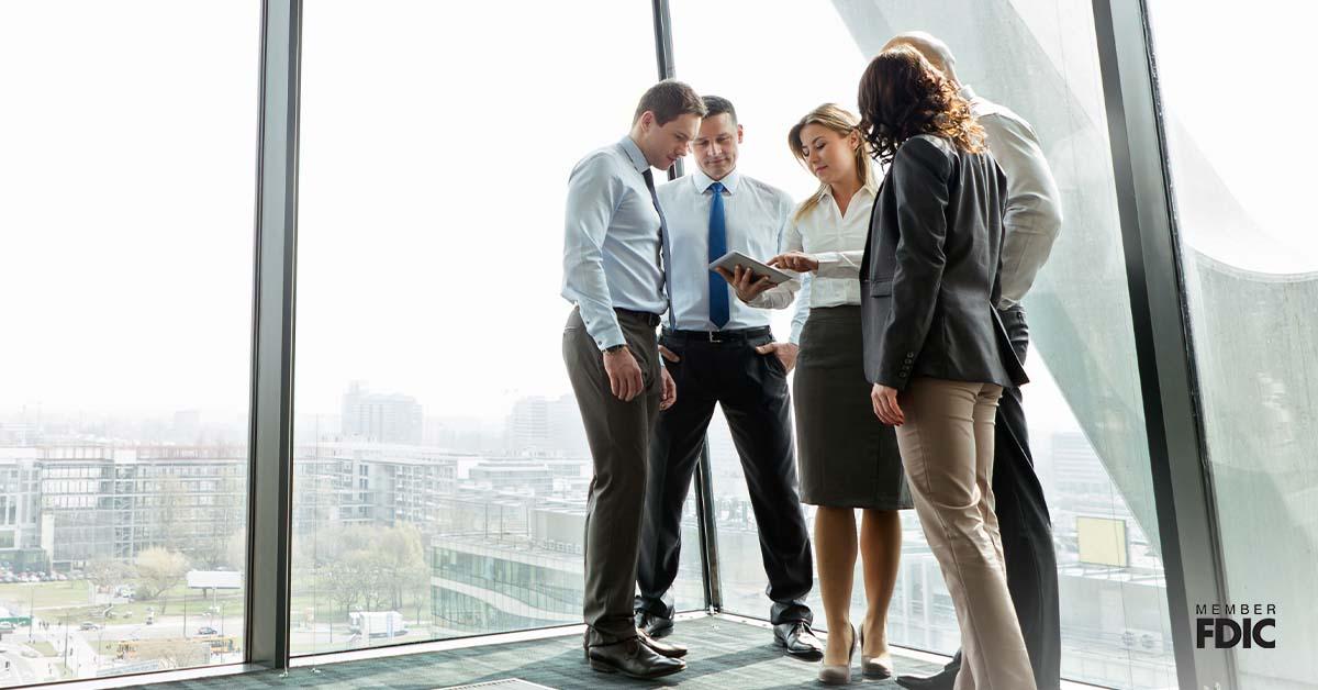 A group of office workers huddle around a digital tablet in a modern lobby.