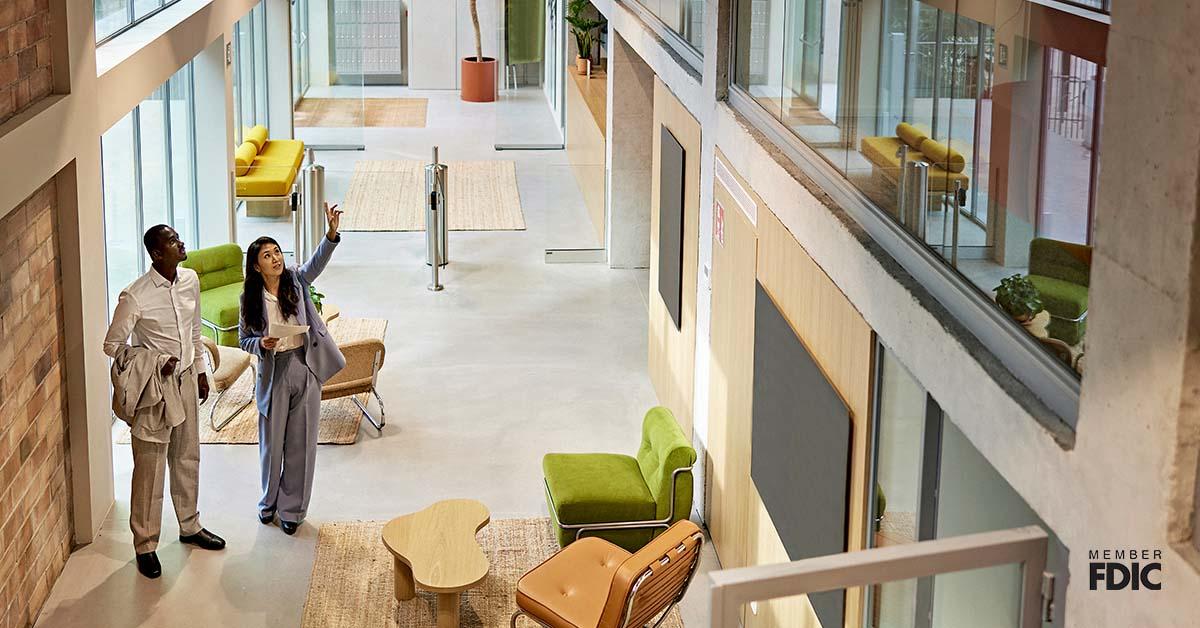 High angle view of female agent standing with male buyer in lobby of modern commercial building for future construction. 