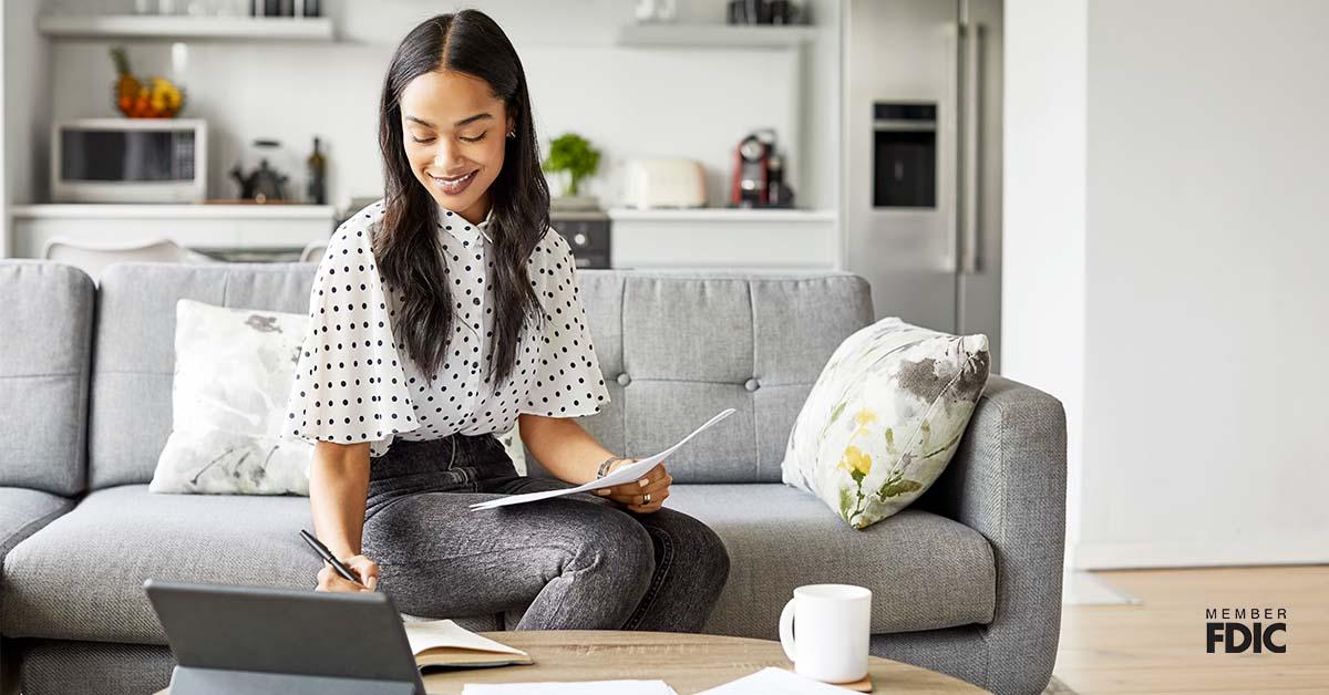 A young adult sits on her couch at home while planning for retirement on her laptop.