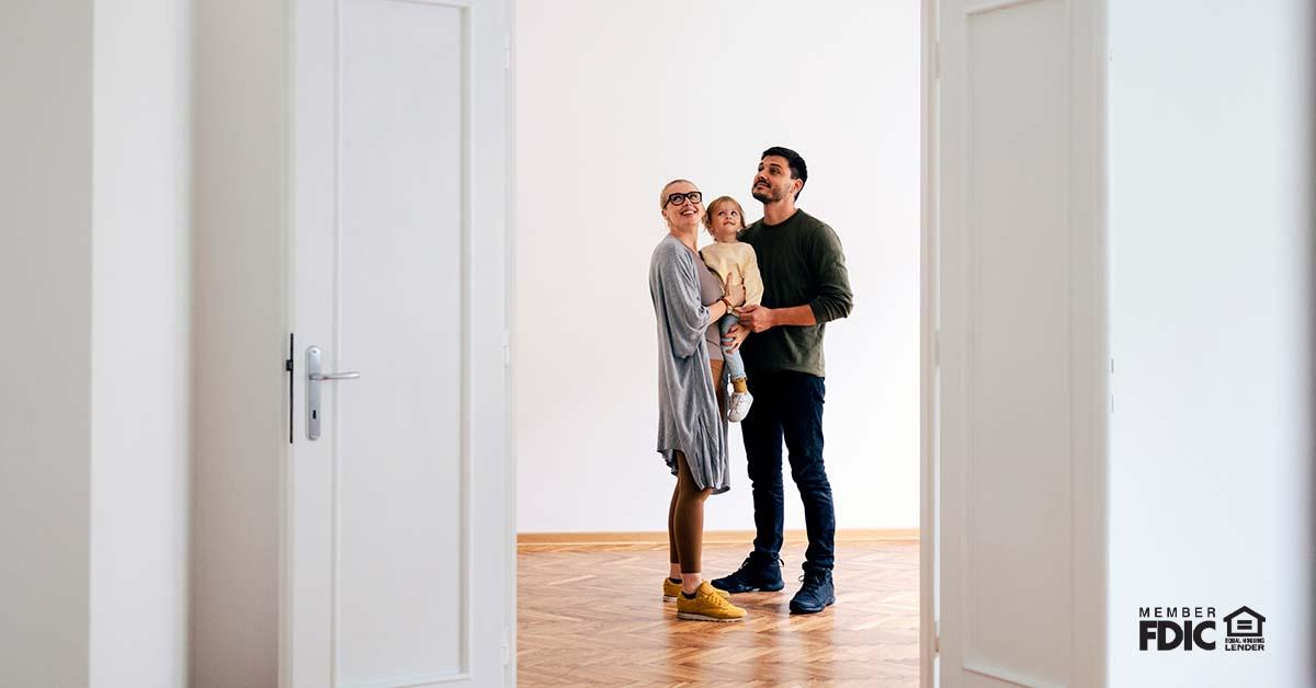 A young mom and dad hold a child in their arms while looking at a brand new home that is up for sale.