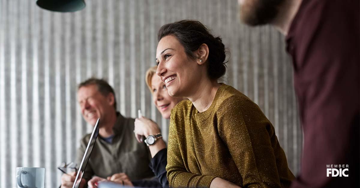 A young professional leans over a conference table with colleagues discussing treasury management services. 