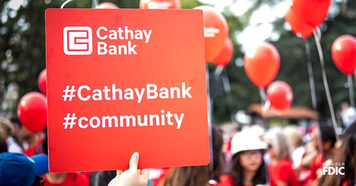 人群中有个人举着一块红色标牌，上面有国泰银行标识以及标着井号的社区和国泰银行标签