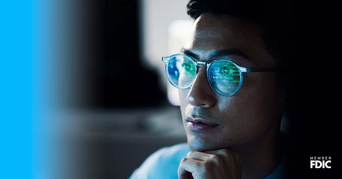 Hay un primer plano del rostro de un joven con lentes, que refleja su actividad en pantalla desde una computadora.