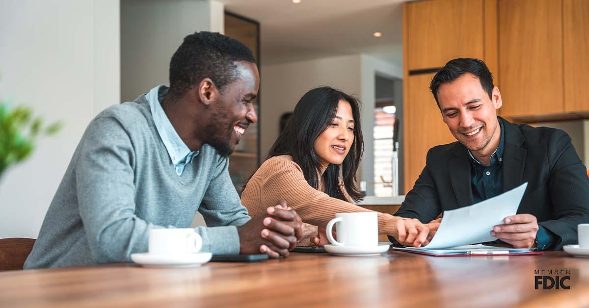 Three adults gather around a kitchen table while looking down at an investment document.