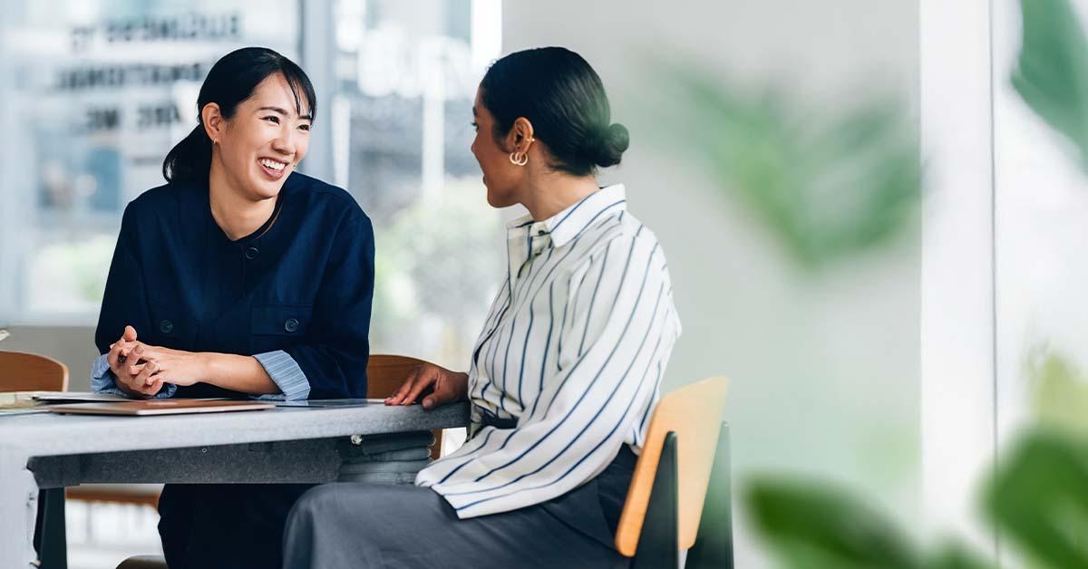 Two professional women sit at a conference table while reviewing financial literacy documents.