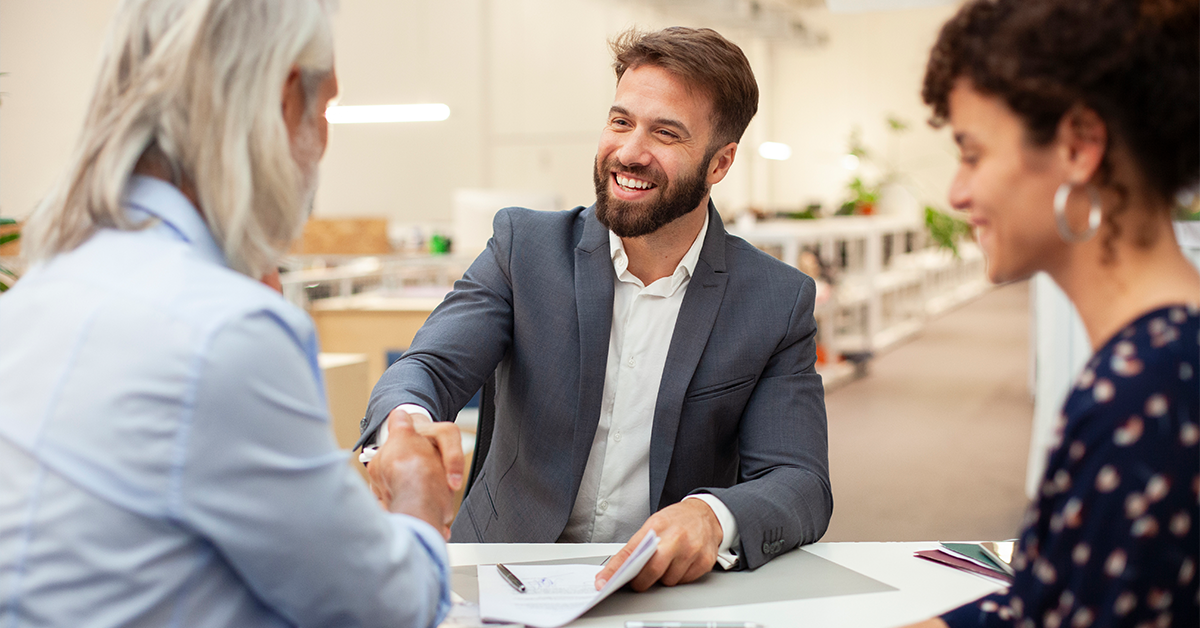Business professional meeting with clients, shaking hands over documents during a discussion on analyzed business checking solutions.