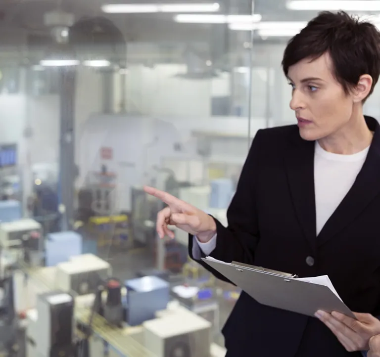 Managers with clipboard looking from window onto factory