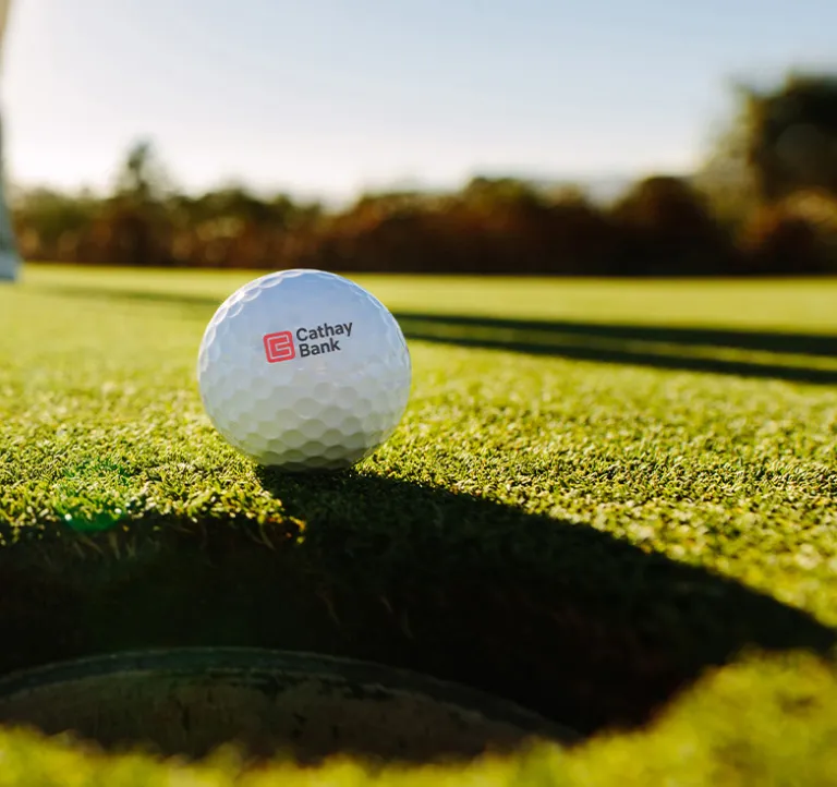 A golf ball with Cathay Bank logo sits outdoors on grass for the annual tournament in California.