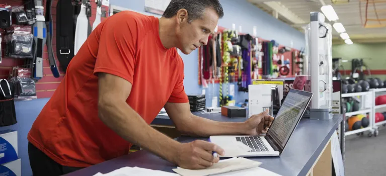 Business owner working at laptop at counter in home gym equipment store
