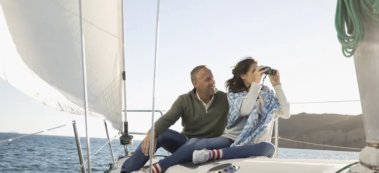 Mature couple using camera on sunny sailboat