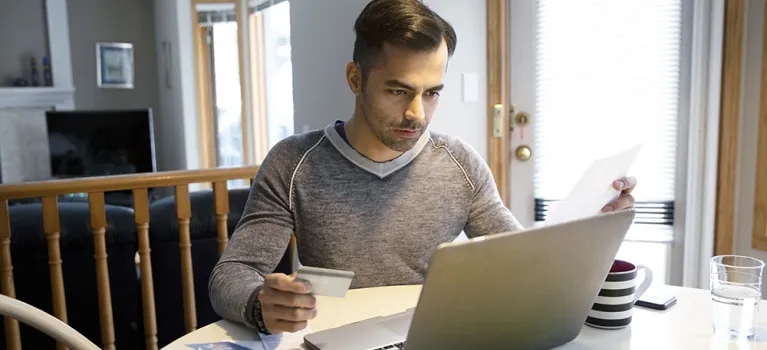 A man with credit card paying bills at laptop