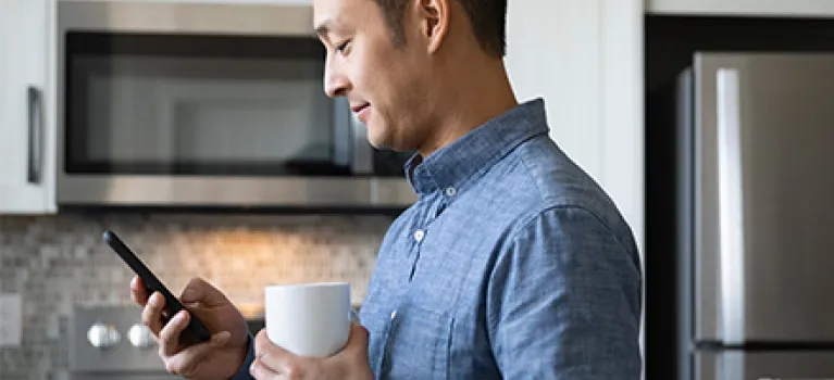 Man drinking coffee and using smart phone in morning kitchen