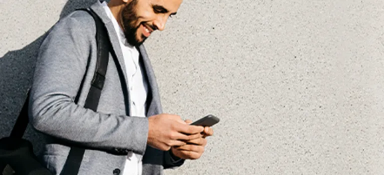Casual young businessman using cell phone at a wall.