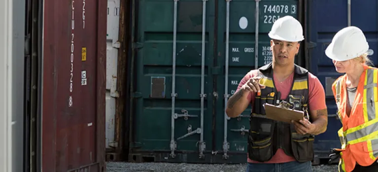Workers inspecting empty shipping container in industrial container yard.