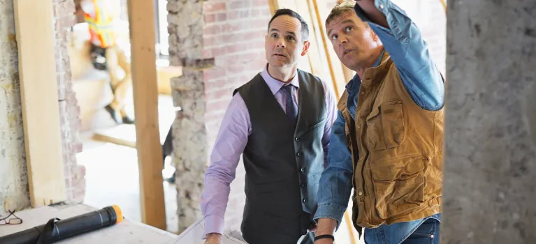 Male architect discussing blueprint with foreman at construction site.