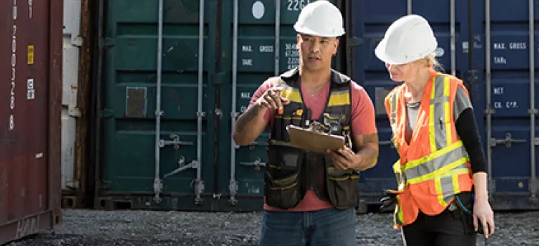 Workers inspecting empty shipping container in industrial container yard.