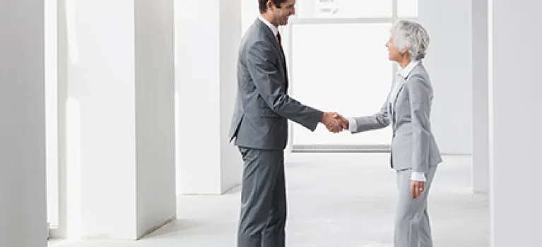 Businessman and businesswoman handshaking in empty office.