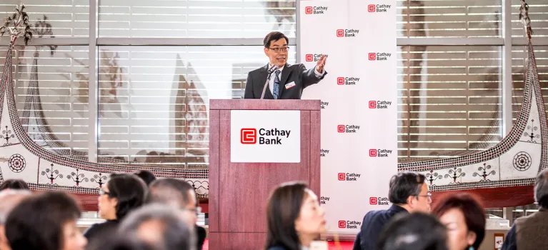 Cathay Bank executive presents behind a podium at the 2018 Economic Outlook Seminar event at Bowers Museum in California.