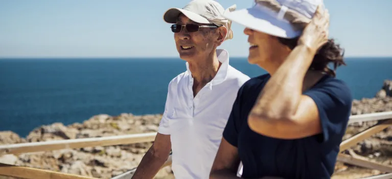 Smiling senior couple looking at sea while standing by railing against clear sky