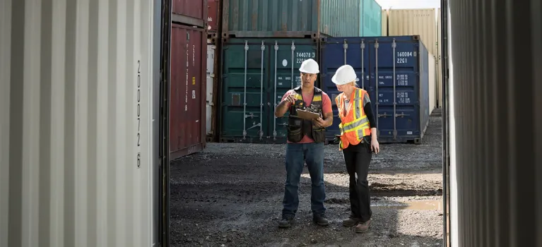 Workers inspecting empty shipping container in industrial container yard.