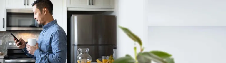 Man drinking coffee and using smart phone in morning kitchen