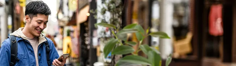 Cheerful young man looking at smartphone in street
