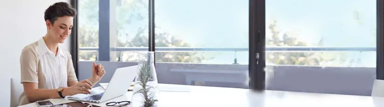 Business woman typing on laptop in meeting room, tablet, phone & glasses on table
