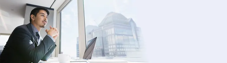 A businessman at laptop looking out urban office window