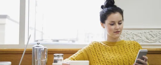 Woman texting and drinking cappuccino in cafe