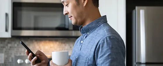 Man drinking coffee and using smart phone in morning kitchen