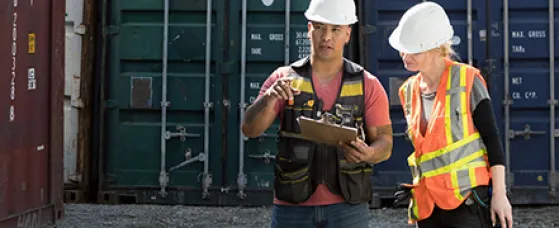 Workers inspecting empty shipping container in industrial container yard.