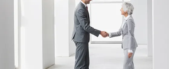 Businessman and businesswoman handshaking in empty office.