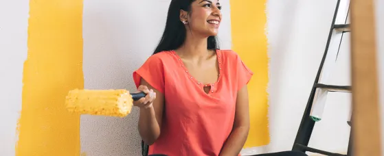 A smiling young woman with paint roller sitting by ladder at home