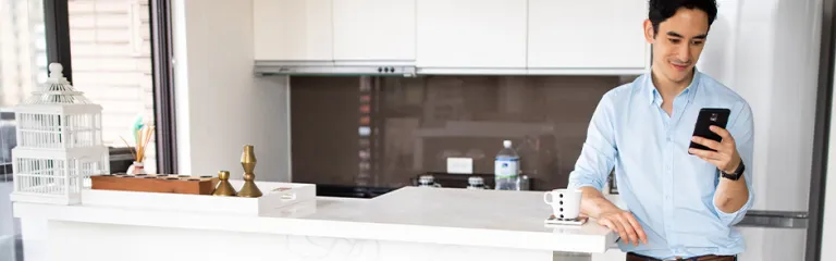 Man standing in the kitchen in modern apartment and using smart phone
