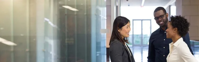 A business woman speaks with a man and a women in a corporate building lobby.