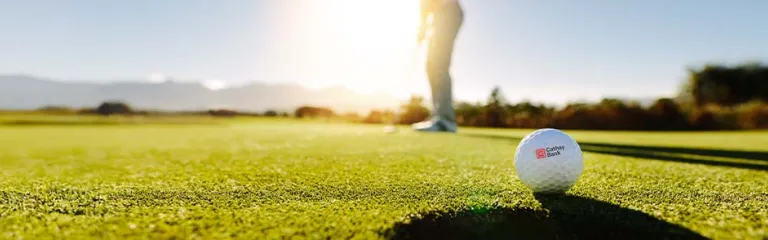 A golf ball with Cathay Bank logo sits outdoors on grass for the annual tournament in California. 