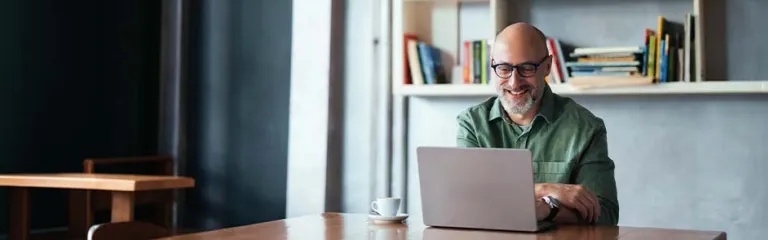 Smiling Man Working on Laptop in Modern Workspace with Bookshelves